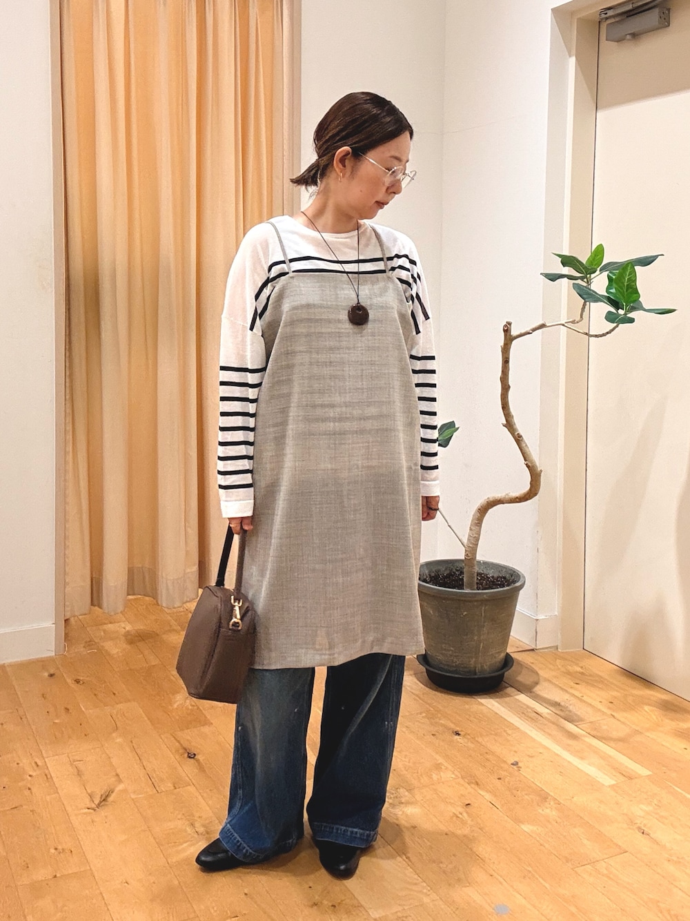 グレー系のワンピース、ブルー系のデニムパンツ、ブラウン系のショルダーバッグを着用したレディースの秋コーディネートの1枚目の写真