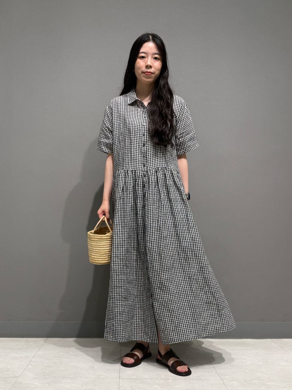 ブラック系のワンピース、ブラウン系のサンダル、ベージュ系のかごバッグを着用したレディースの夏コーディネートの1枚目の写真