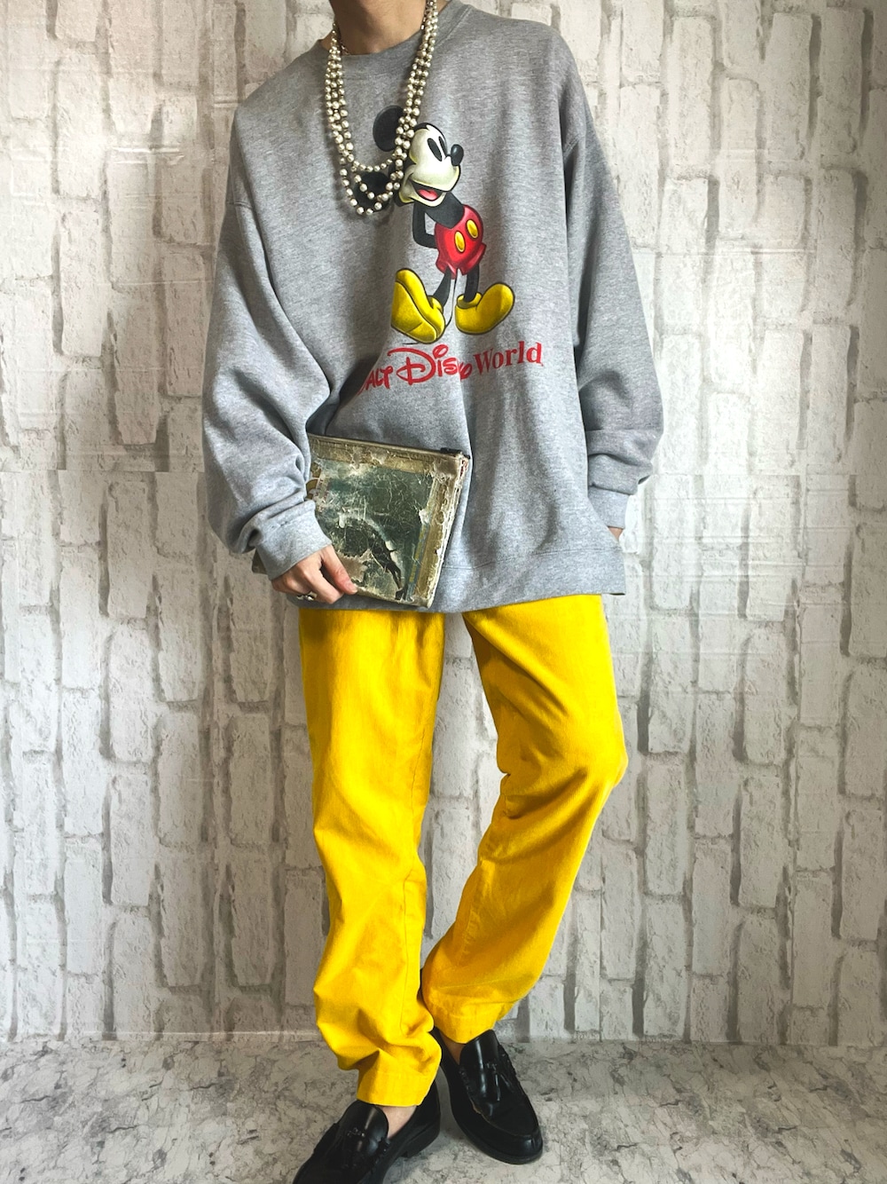 グレー系のスウェット、ベージュ系のクラッチバッグ、イエロー系のパンツを着用したメンズの春コーディネートの1枚目の写真