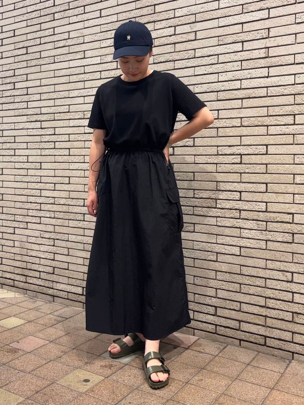 ブラック系のワンピース、グリーン系のサンダル、ブルー系のキャップを着用したレディースの夏コーディネートの1枚目の写真