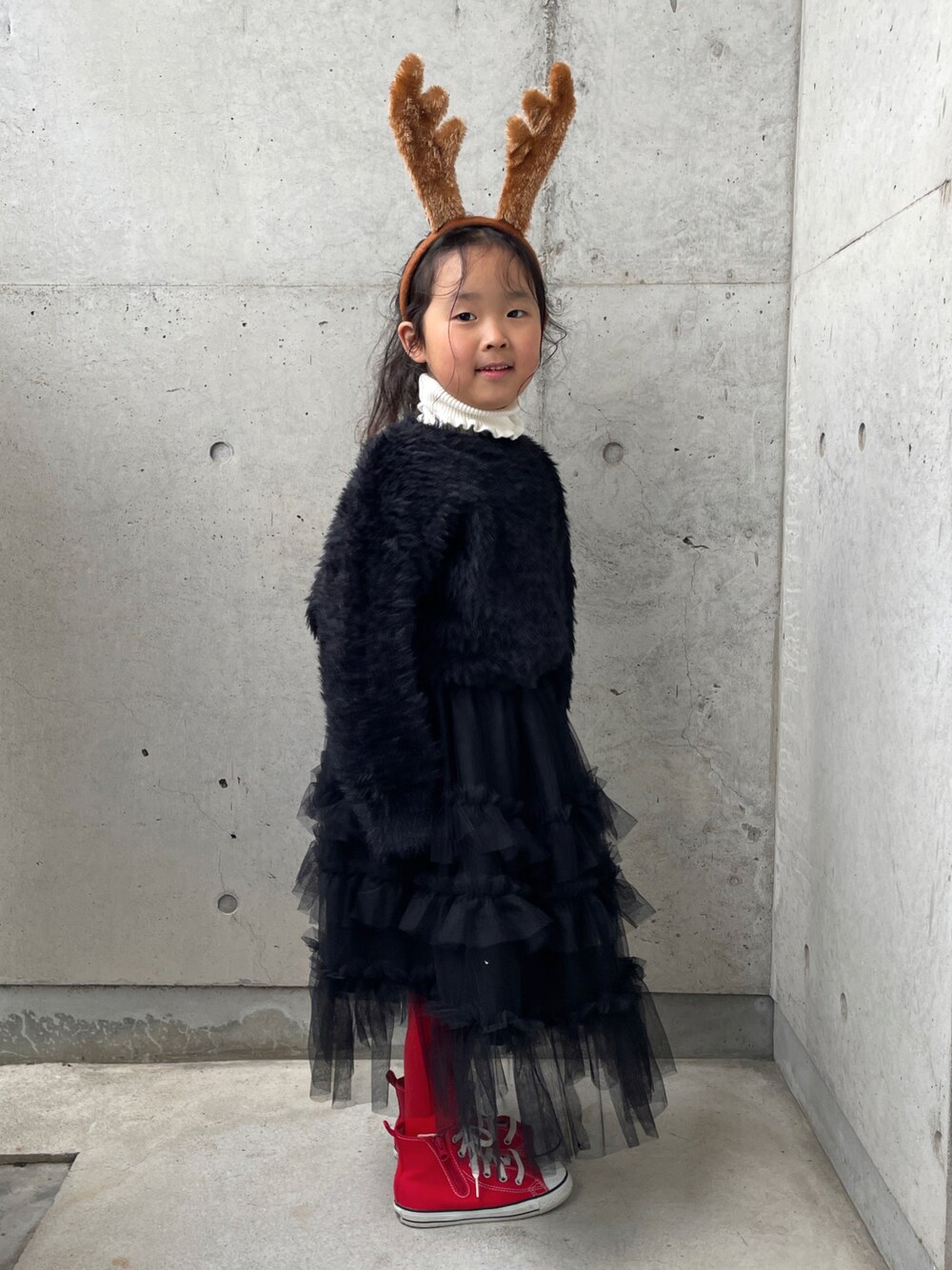 ブラック系のスカート、ホワイト系のニット/セーター、レッド系のスニーカーを着用したキッズの冬コーディネートの1枚目の写真