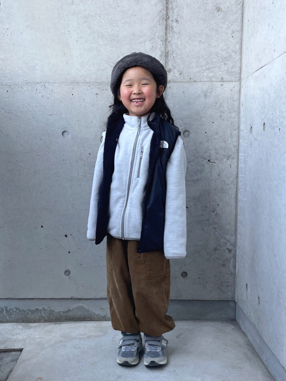 グレー系のトップス、ブラック系のベスト、イエロー系のその他パンツを着用したキッズの冬コーディネートの1枚目の写真