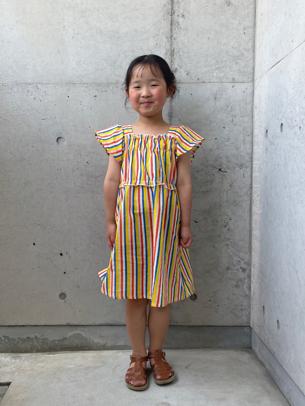 ベージュ系のサンダル、イエロー系のワンピースを着用したキッズの春コーディネートの1枚目の写真