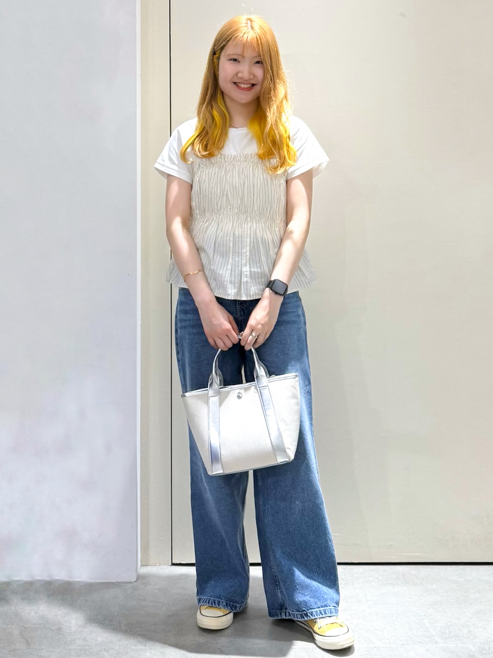 ブルー系のデニムパンツ、シルバー系のトートバッグ、ベージュ系のTシャツ/カットソーを着用したレディースの春コーディネートの1枚目の写真