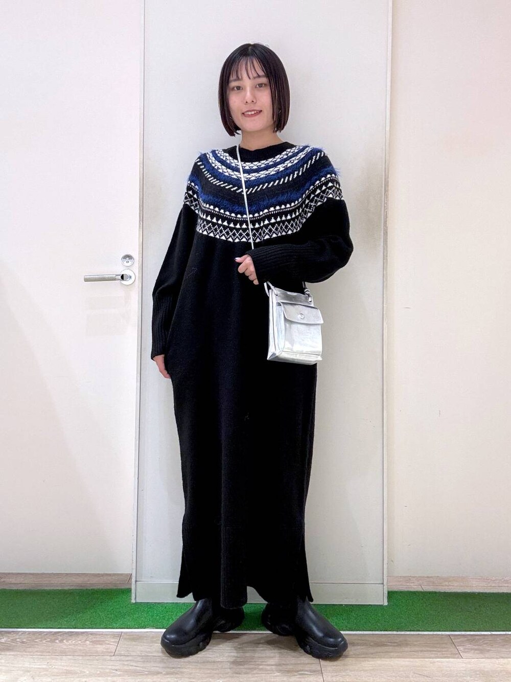 シルバー系のショルダーバッグ、ブラック系のブーツ、ブラック系のワンピースを着用したレディースの秋コーディネートの1枚目の写真