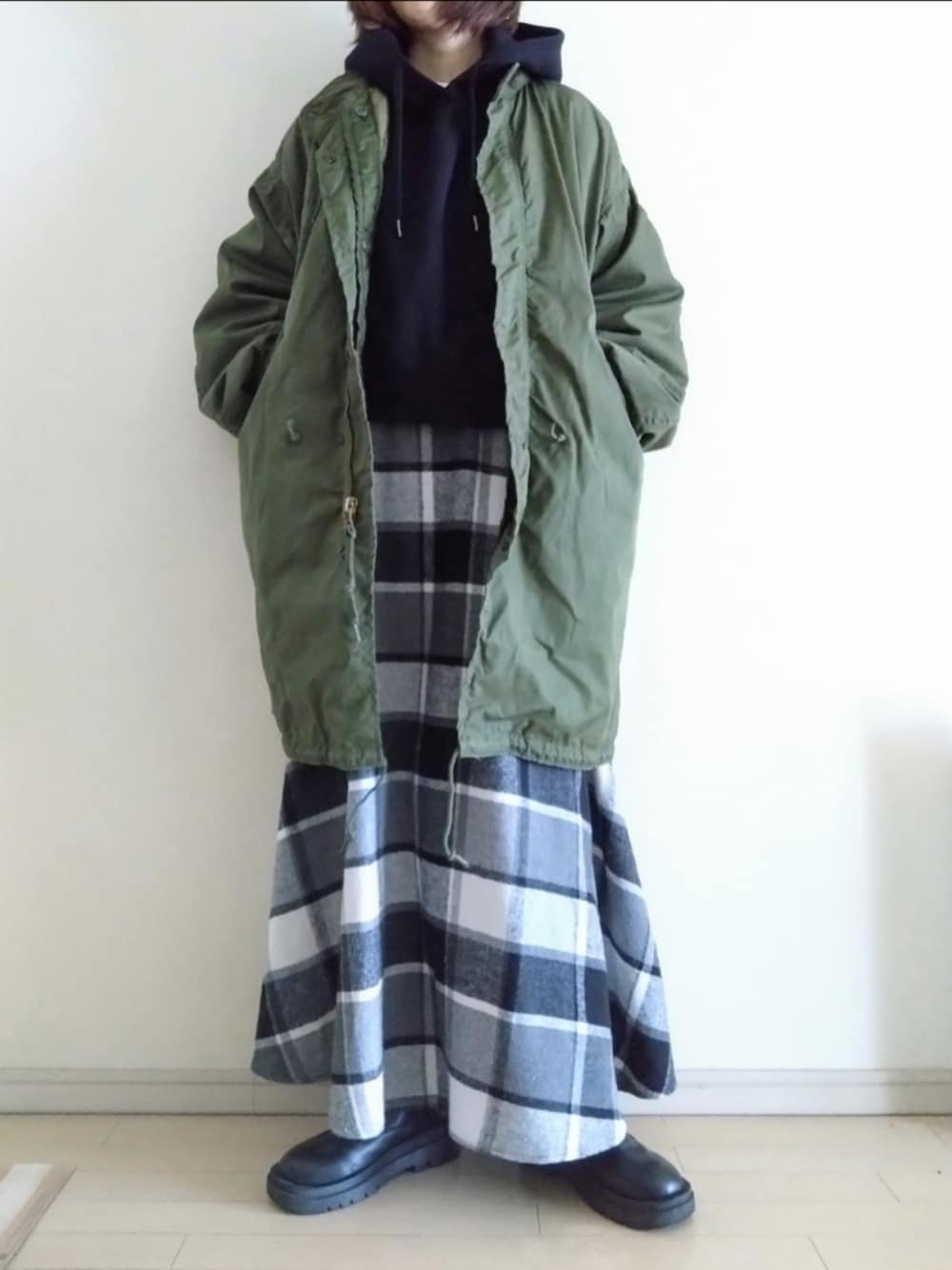 グリーン系のモッズコート、ブラック系のパーカー、ブラック系のスカートを着用したレディースの冬コーディネートの1枚目の写真