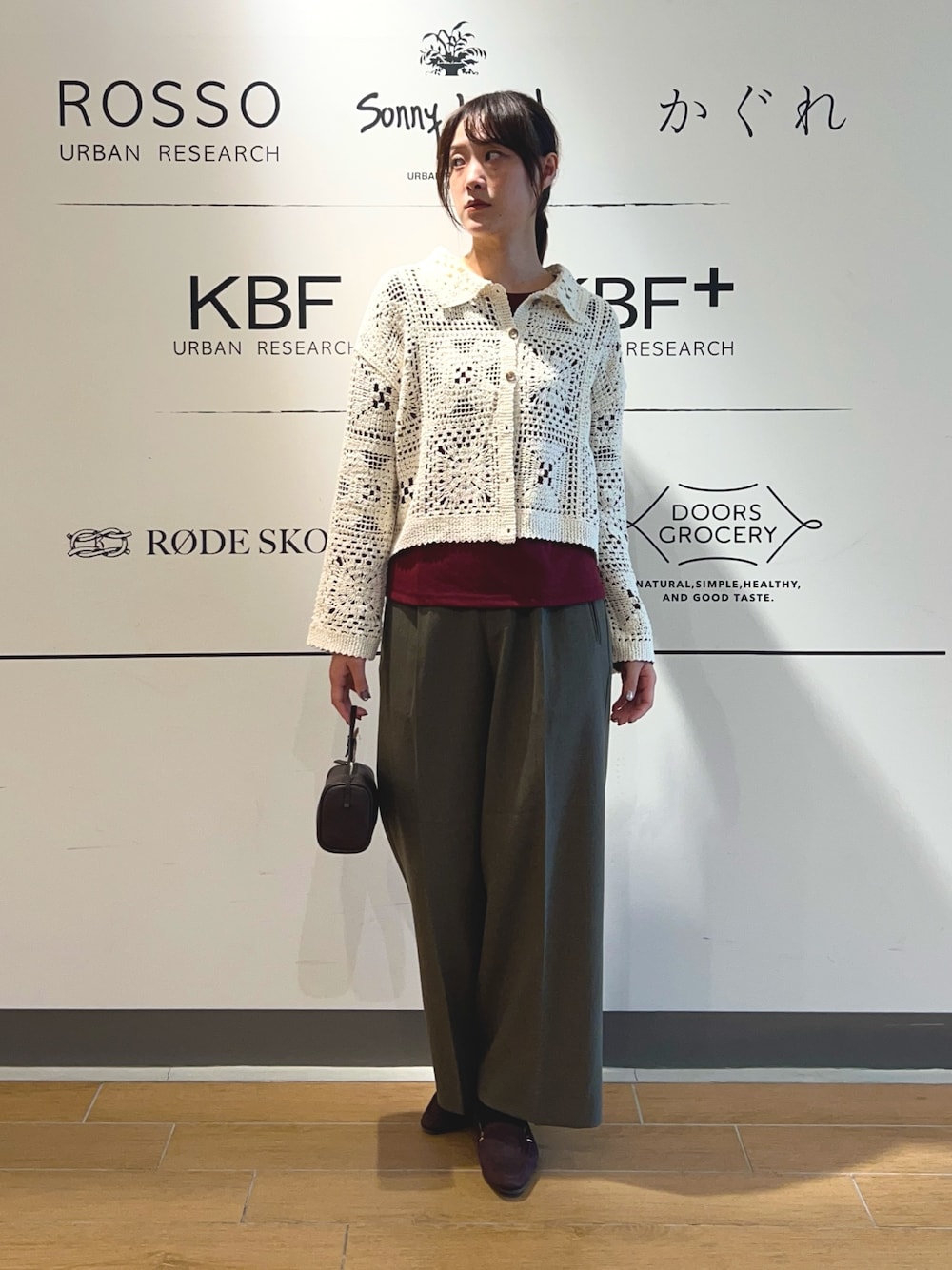 レッド系のTシャツ/カットソー、ベージュ系のカーディガン/ボレロ、ブラウン系のハンドバッグを着用したレディースの秋コーディネートの1枚目の写真