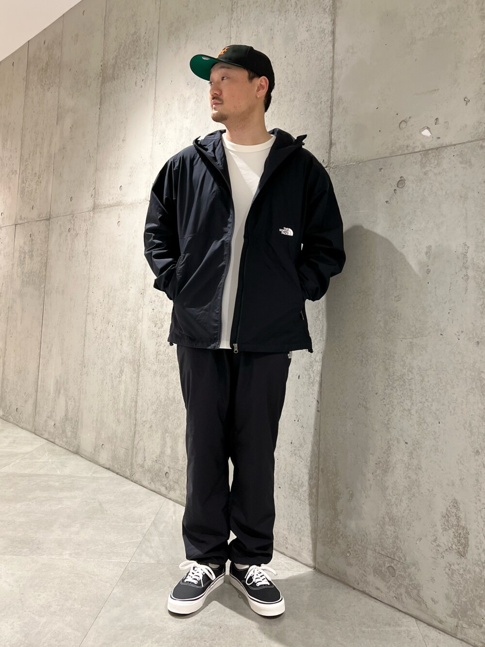 ブラック系のマウンテンパーカー、ホワイト系のTシャツ/カットソー、ブラック系のスニーカーを着用したメンズの春コーディネートの1枚目の写真