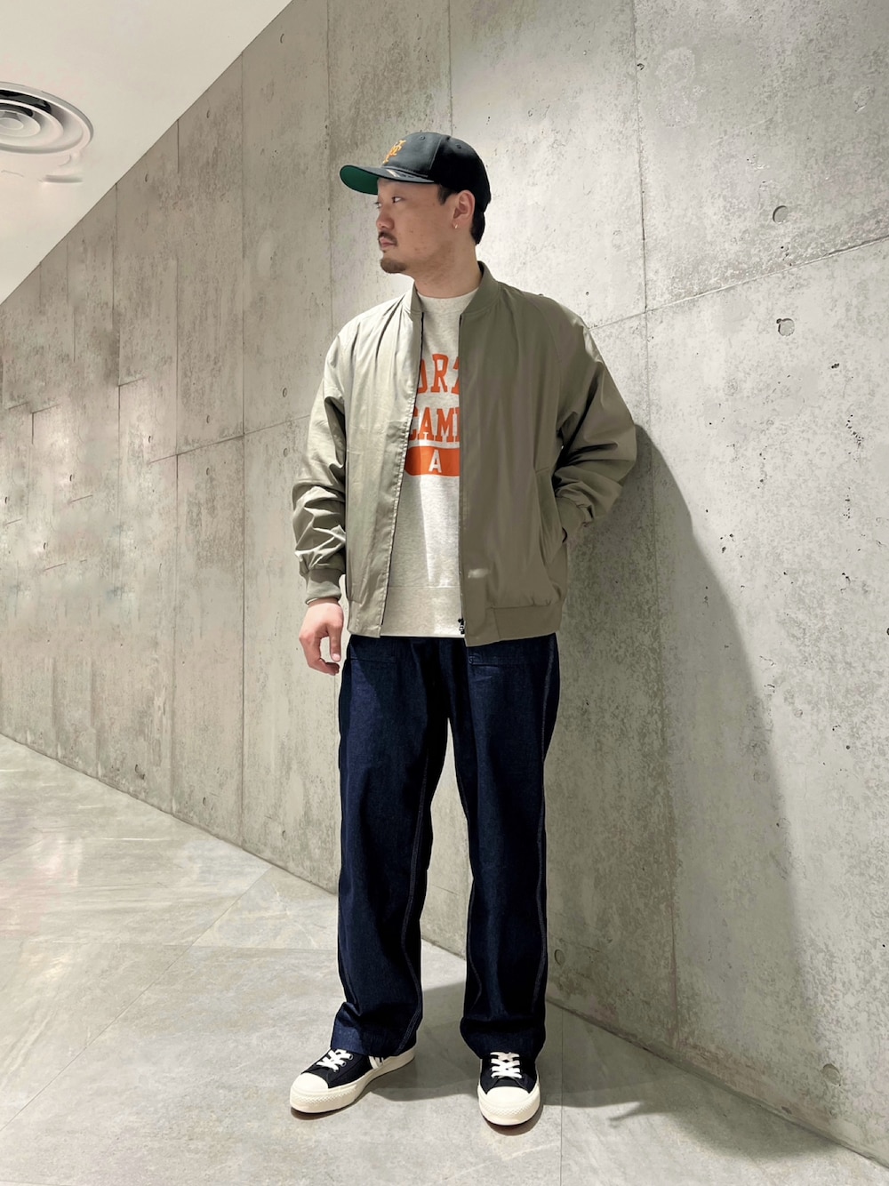 グリーン系のブルゾン、ベージュ系のTシャツ/カットソー、ブルー系のデニムパンツを着用したメンズの春コーディネートの1枚目の写真