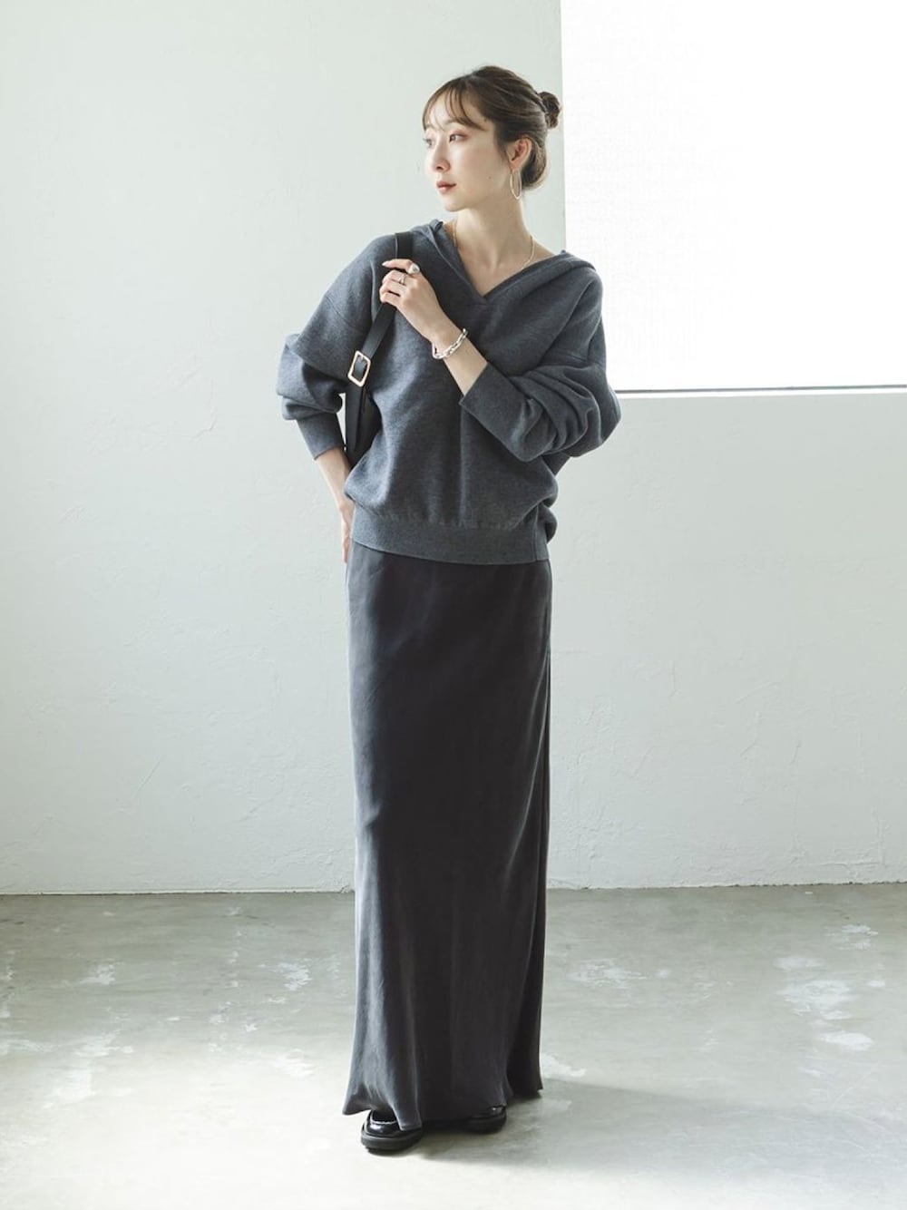 グレー系のニット/セーター、グレー系のスカート、ブラック系のショルダーバッグを着用したレディースの秋コーディネートの1枚目の写真