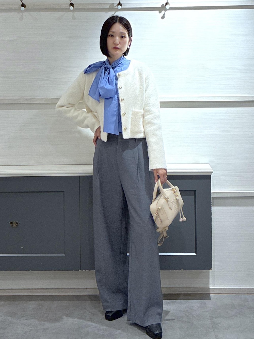 ピンク系のボストンバッグ、グレー系のスラックス、ホワイト系のカーディガン/ボレロを着用したレディースの冬コーディネートの1枚目の写真