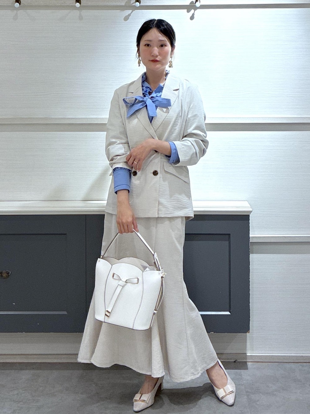 ホワイト系のショルダーバッグ、ベージュ系のパンプス、ブルー系のシャツ/ブラウスを着用したレディースの春コーディネートの1枚目の写真