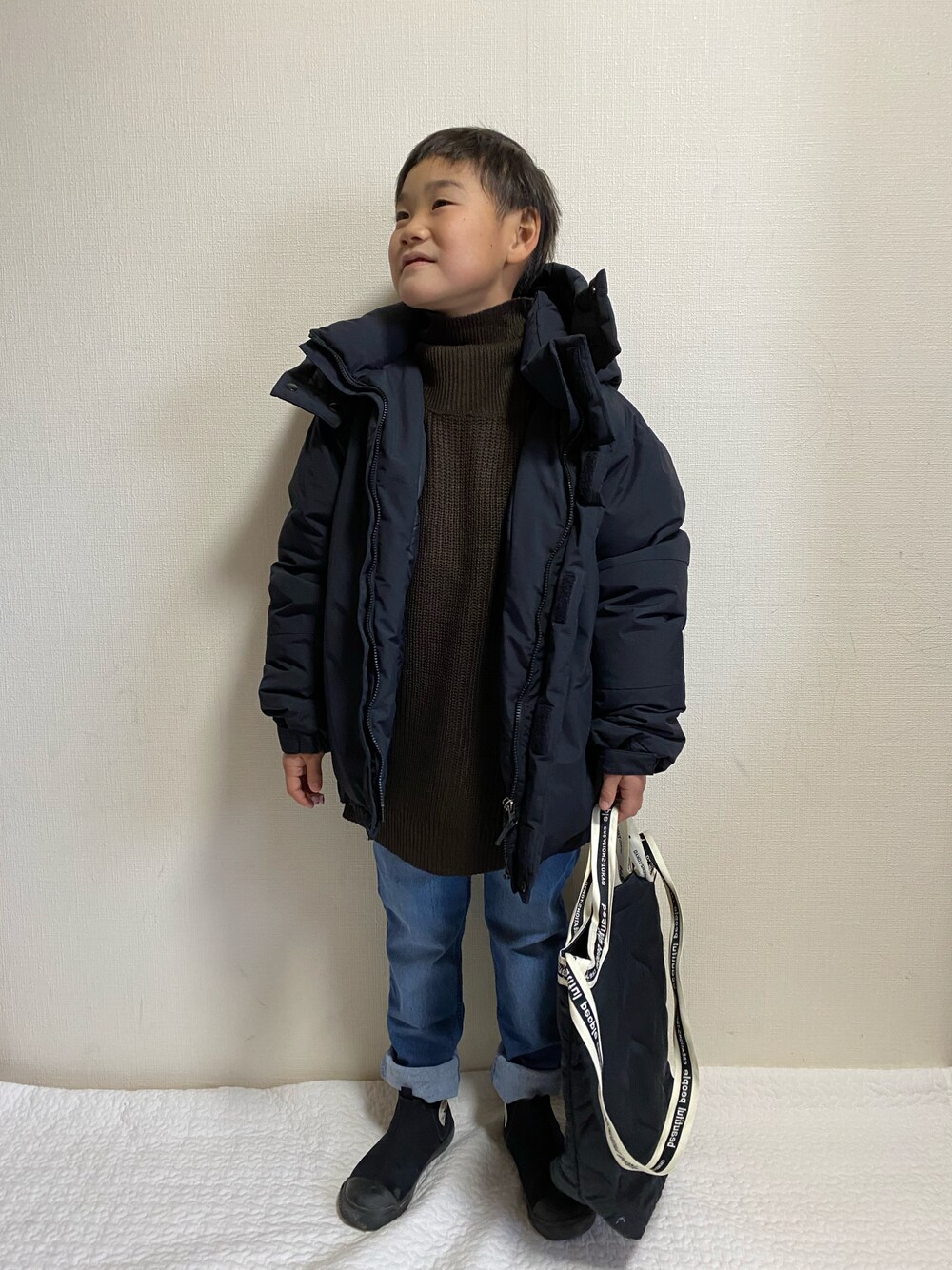 ブラック系のダウンジャケット/コート、ブラウン系のニット/セーター、ブルー系のデニムパンツを着用したキッズの冬コーディネートの1枚目の写真