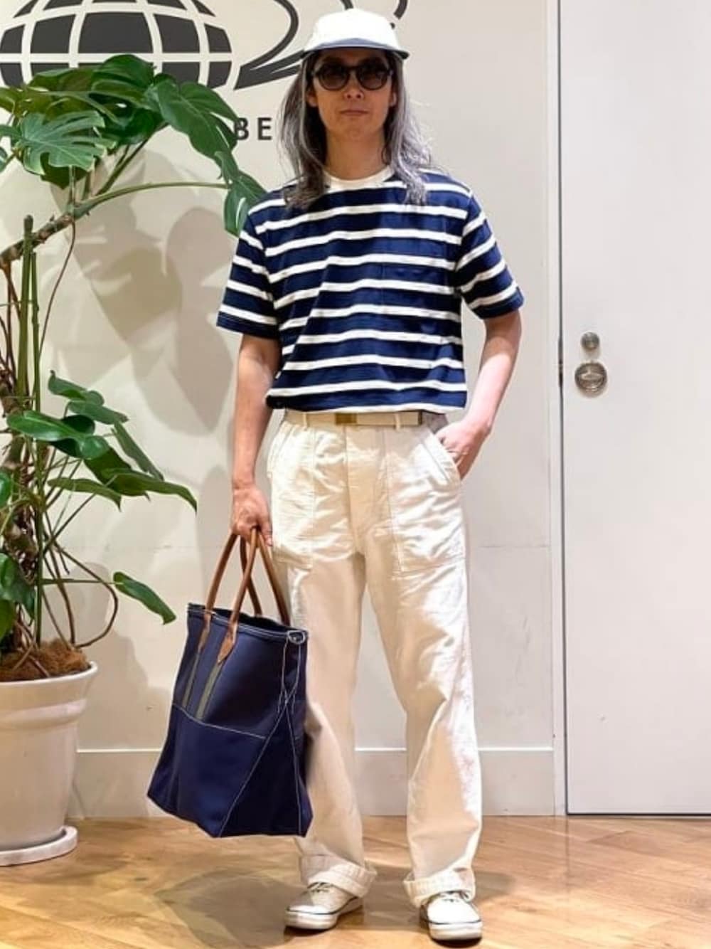 ブルー系のトートバッグ、ブルー系のTシャツ/カットソー、ホワイト系のキャップを着用したメンズの夏コーディネートの1枚目の写真