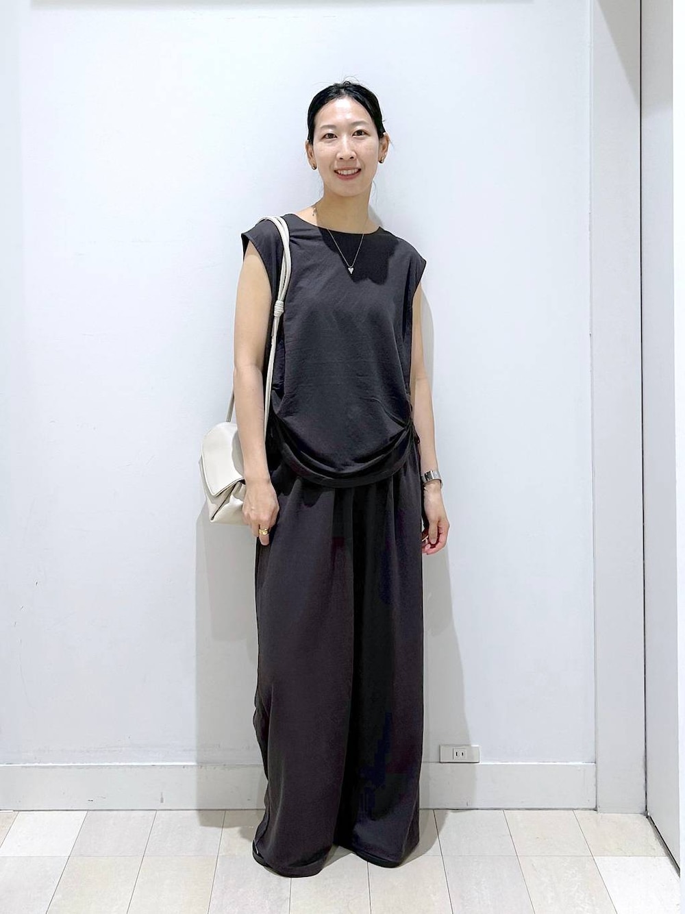 ベージュ系のショルダーバッグ、ブラック系のTシャツ/カットソー、ベージュ系のサンダルを着用したレディースの夏コーディネートの1枚目の写真