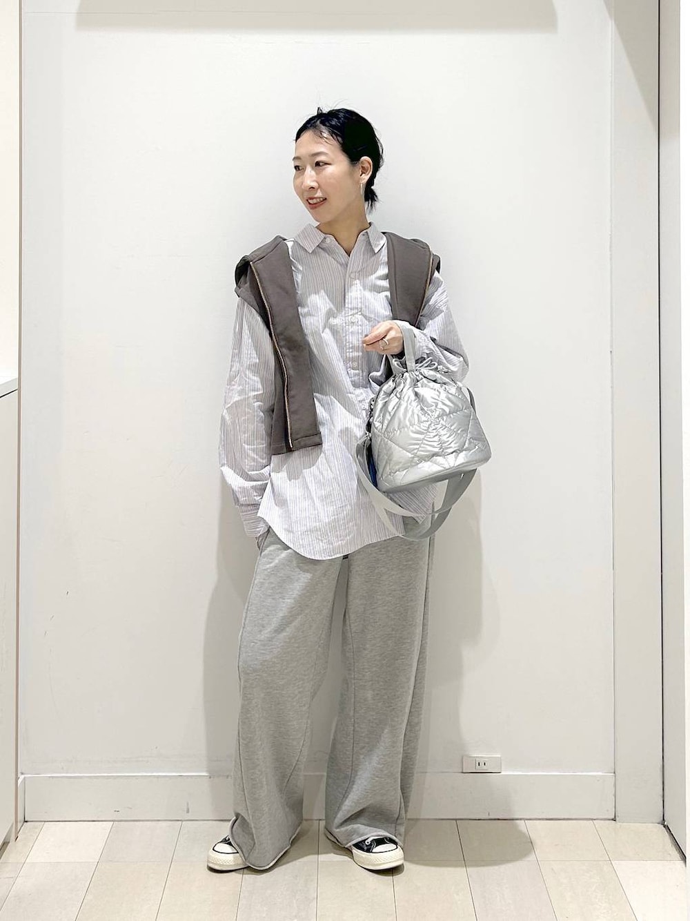 シルバー系のハンドバッグ、グレー系のスウェットパンツ、ブラウン系のベストを着用したレディースの春コーディネートの1枚目の写真