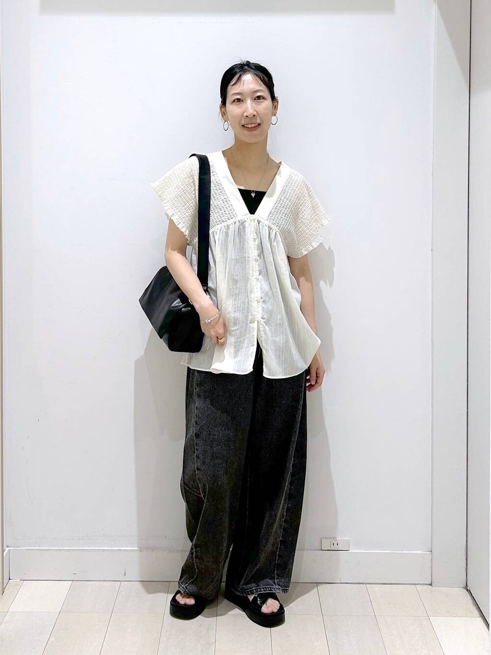 ブラック系のデニムパンツ、ベージュ系のシャツ/ブラウス、ブラック系のサンダルを着用したレディースの夏コーディネートの1枚目の写真