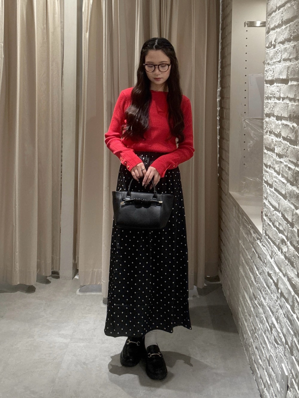 レッド系のニット/セーター、ブラック系のスカート、ブラウン系のサングラスを着用したレディースの秋コーディネートの1枚目の写真