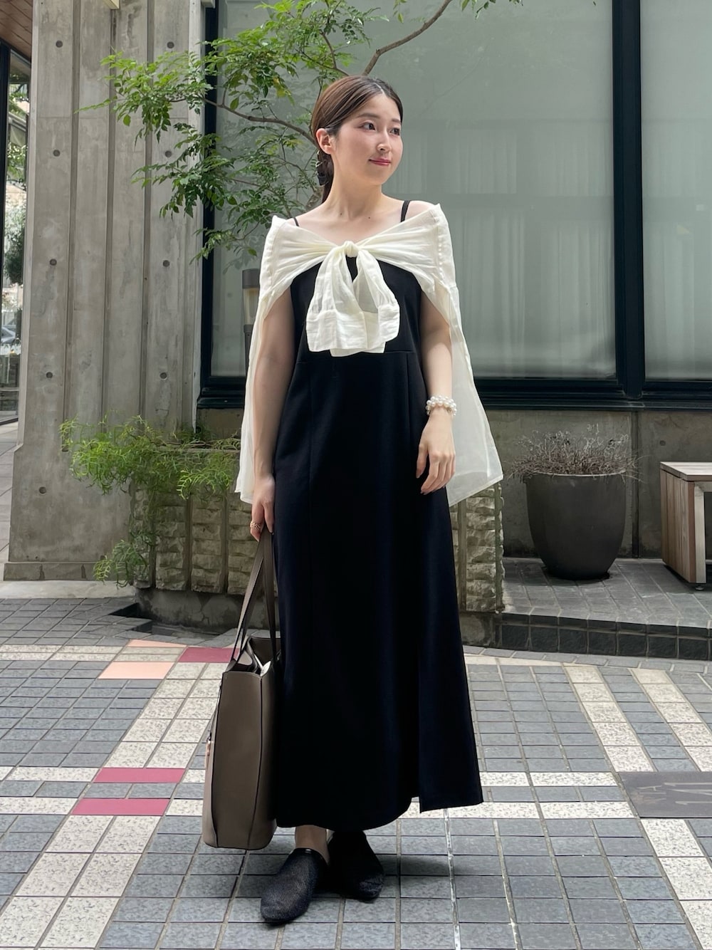 ベージュ系のビジネスバッグ、ホワイト系のシャツ/ブラウス、ブラック系のジャンパースカートを着用したレディースの夏コーディネートの1枚目の写真