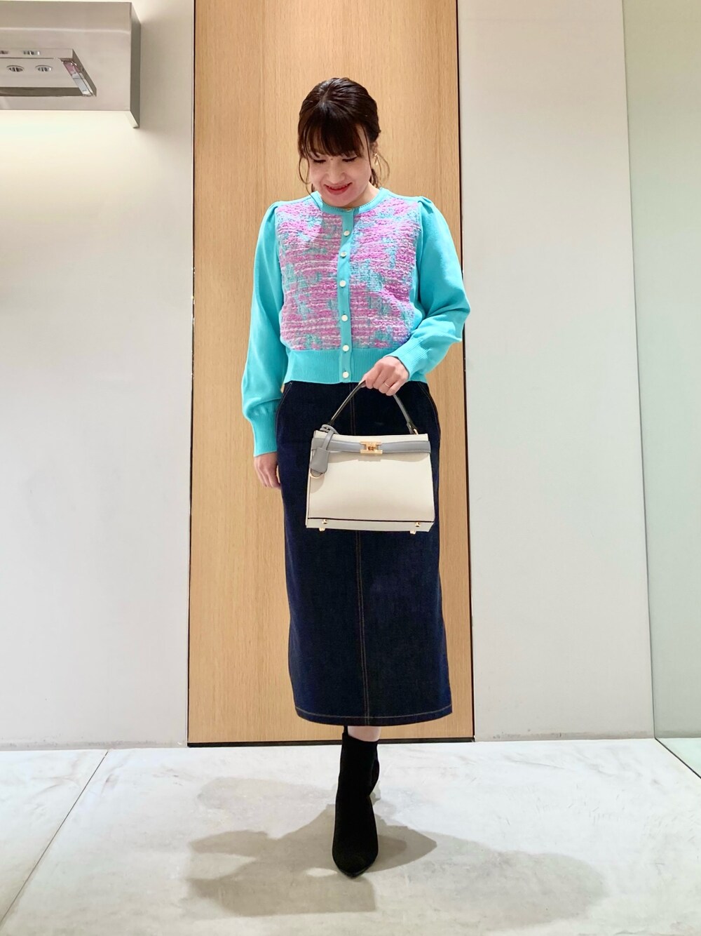 グリーン系のカーディガン/ボレロ、ホワイト系のハンドバッグ、ブルー系のデニムスカートを着用したレディースの冬コーディネートの1枚目の写真