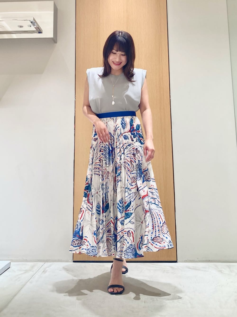 グレー系のニット/セーター、ブルー系のスカート、ホワイト系のネックレスを着用したレディースの夏コーディネートの1枚目の写真