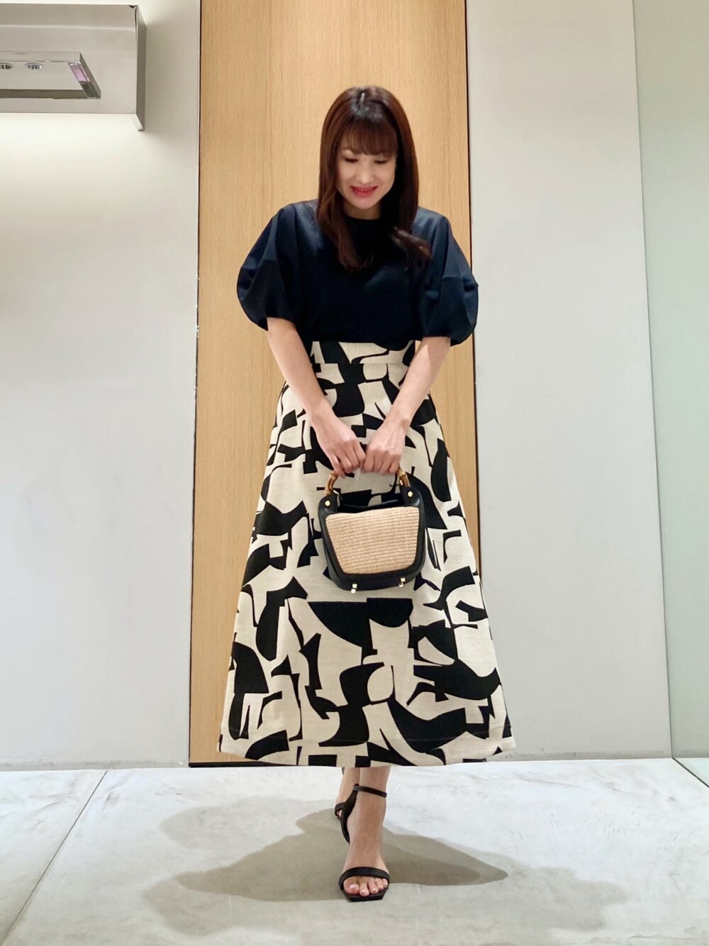 ブラック系のTシャツ/カットソー、ベージュ系のスカート、ブラック系のハンドバッグを着用したレディースの春コーディネートの1枚目の写真