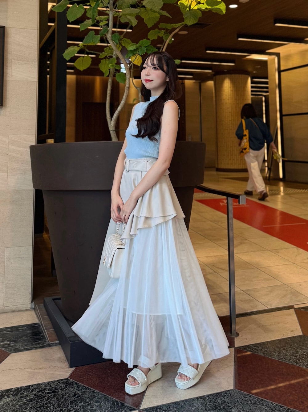 ベージュ系のスカート、ブルー系のニット/セーター、ホワイト系のショルダーバッグを着用したレディースの夏コーディネートの1枚目の写真