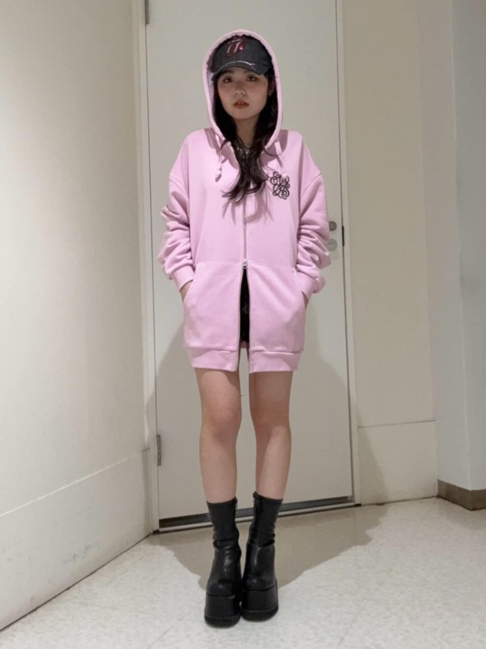 ブラック系のブーツ、ピンク系のパーカー、ブラック系のキャップを着用したレディースの春コーディネートの1枚目の写真