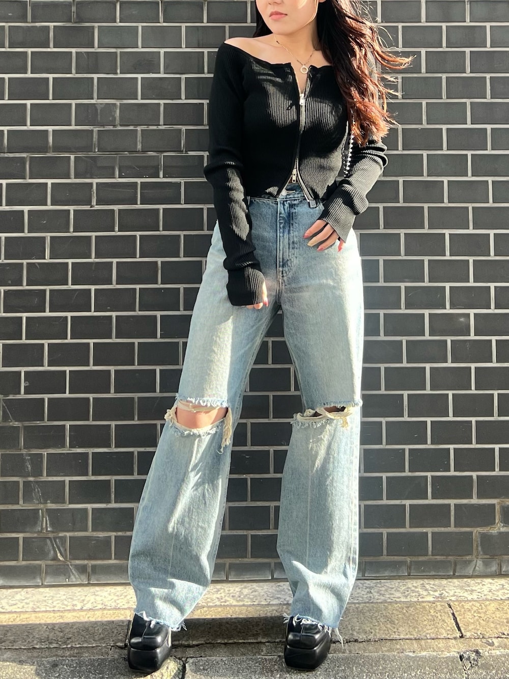 ブルー系のデニムパンツ、ブラック系のニット/セーター、ブラック系のサンダルを着用したレディースの春コーディネートの1枚目の写真