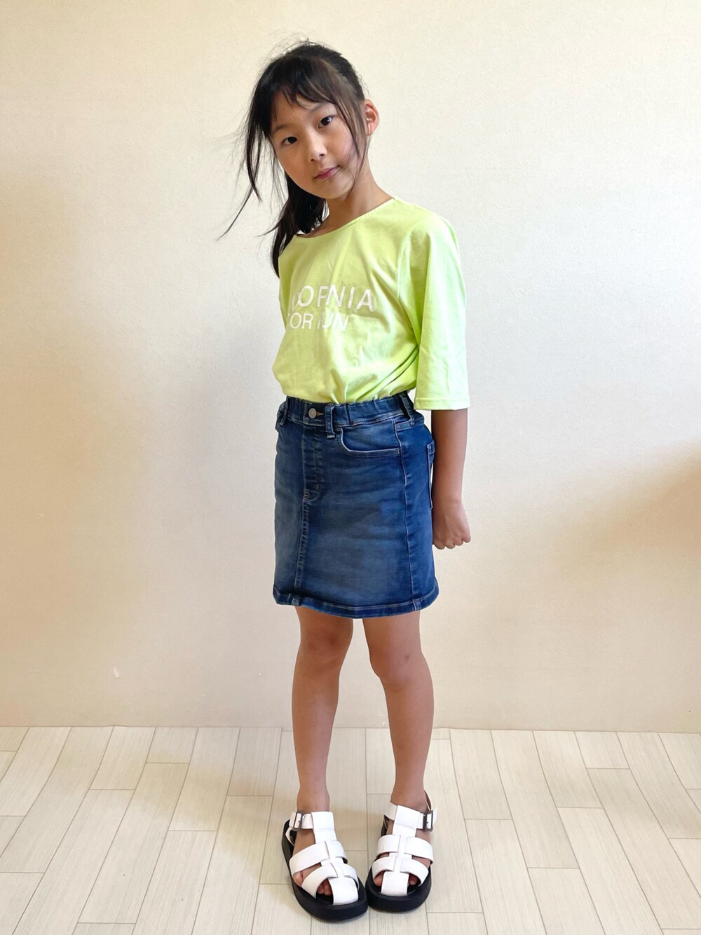 グリーン系のTシャツ/カットソー、ブルー系のデニムスカート、ホワイト系のサンダルを着用したキッズの夏コーディネートの1枚目の写真
