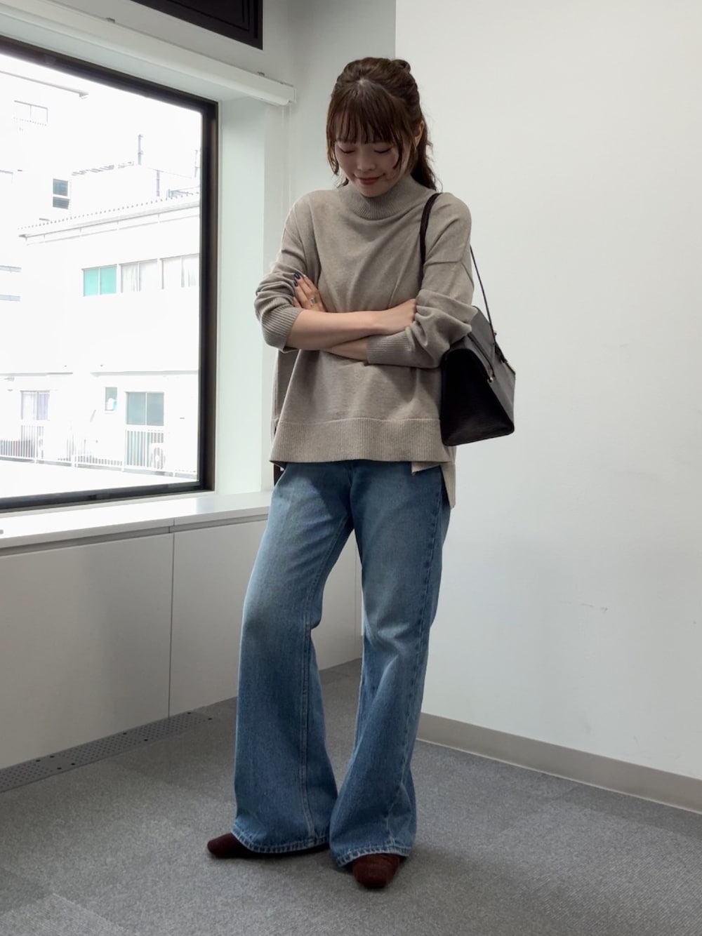 ブルー系のデニムパンツ、ベージュ系のニット/セーター、ブラウン系のトートバッグを着用したレディースの秋コーディネートの1枚目の写真