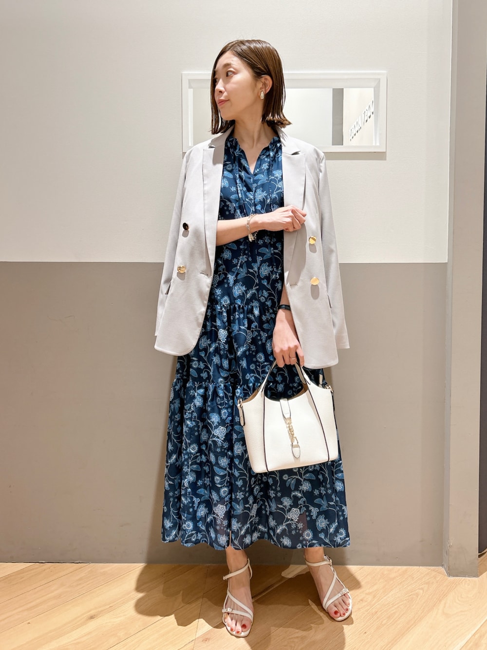 ベージュ系のテーラードジャケット、ブルー系のワンピース、ホワイト系のエコバッグ/サブバッグを着用したレディースの春コーディネートの1枚目の写真