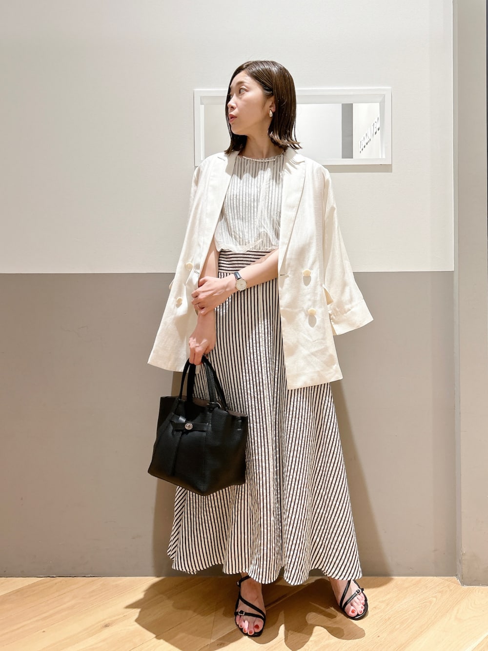 ホワイト系のテーラードジャケット、ホワイト系のワンピース、ブラック系のサンダルを着用したレディースの春コーディネートの1枚目の写真