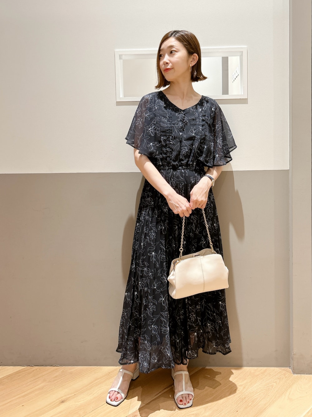 ブラック系のワンピース、ホワイト系のサンダル、ベージュ系のクラッチバッグを着用したレディースの夏コーディネートの1枚目の写真