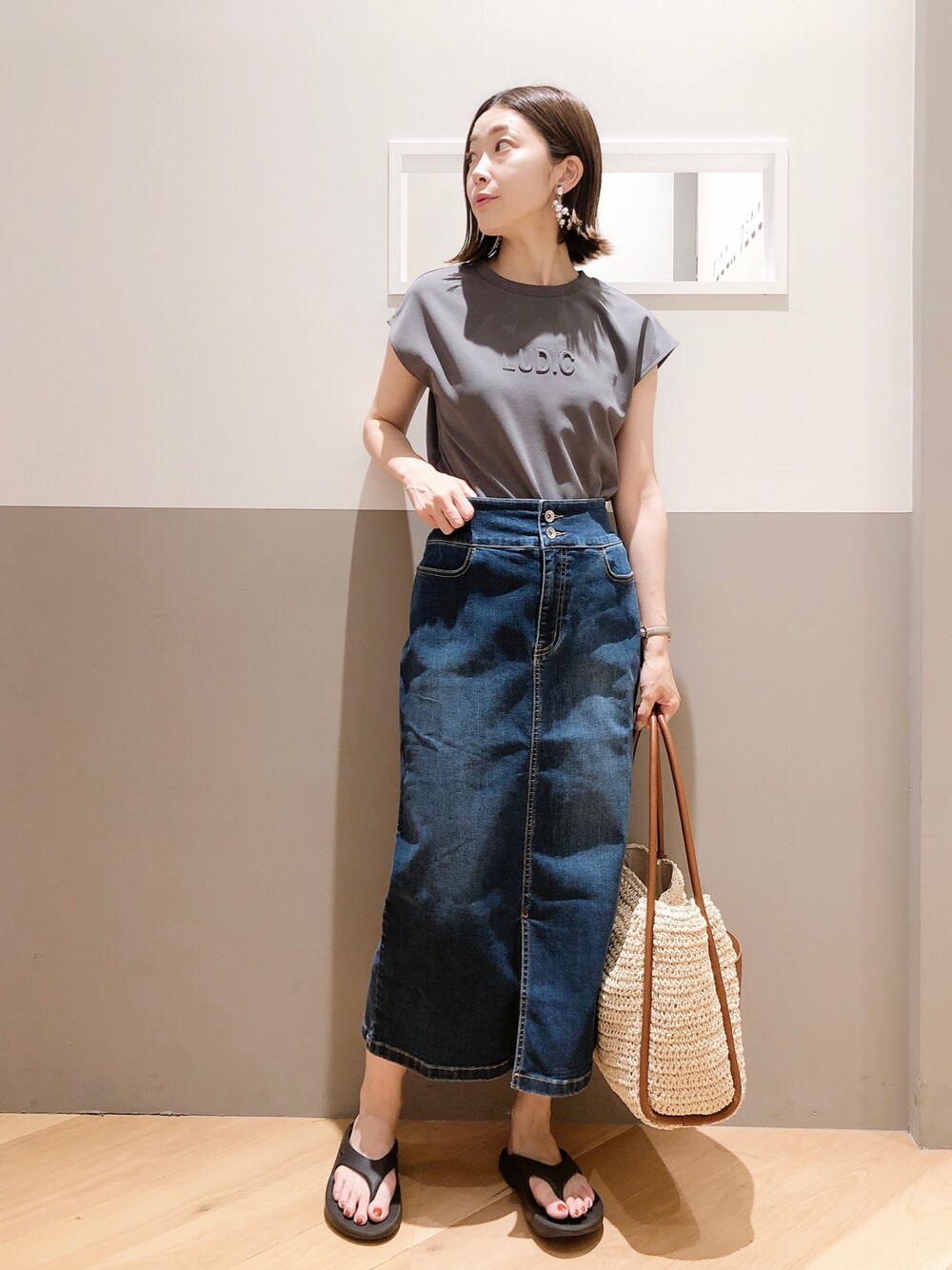 グレー系のトップス、ブルー系のスカート、ブラウン系のトートバッグを着用したレディースの夏コーディネートの1枚目の写真