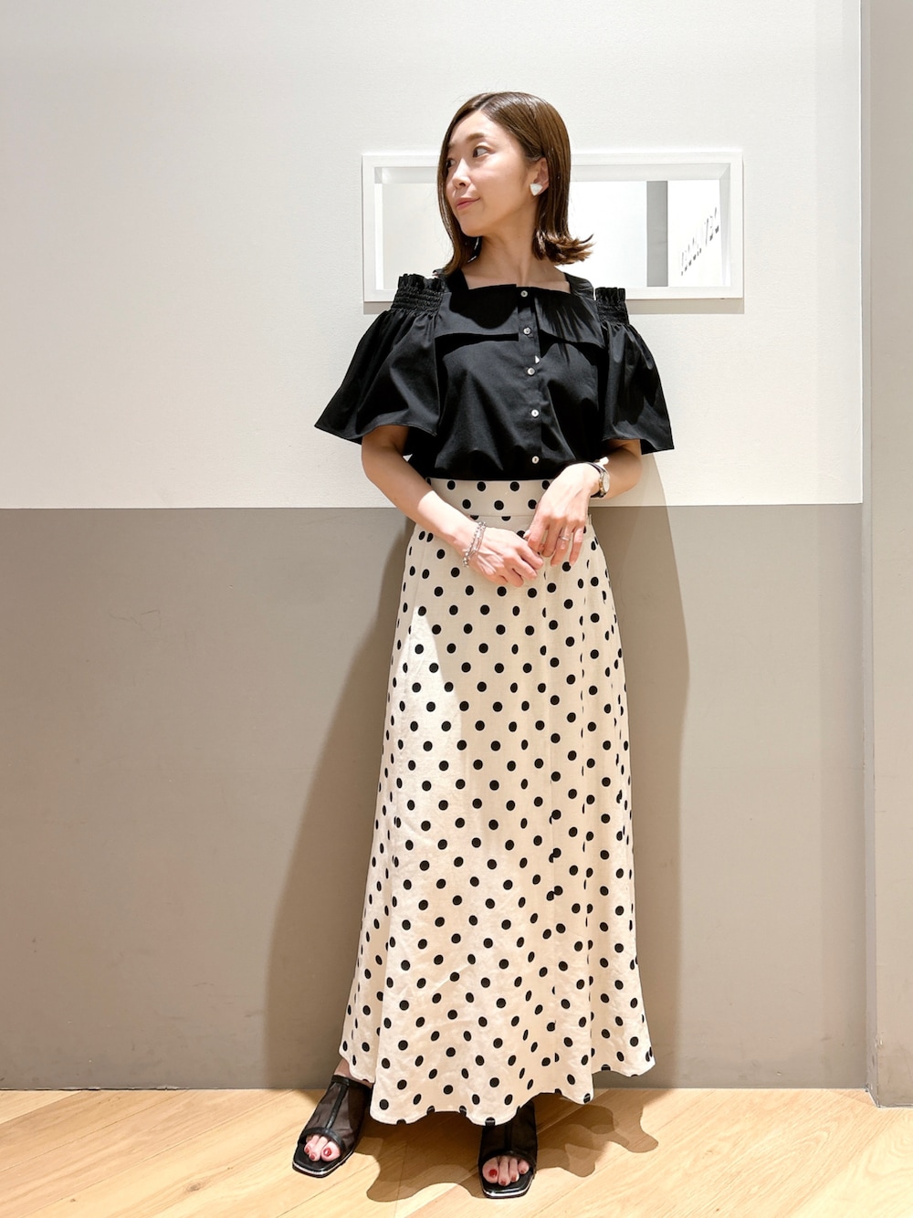 ブラック系のシャツ/ブラウス、ベージュ系のスカート、ブラック系のサンダルを着用したレディースの春コーディネートの1枚目の写真