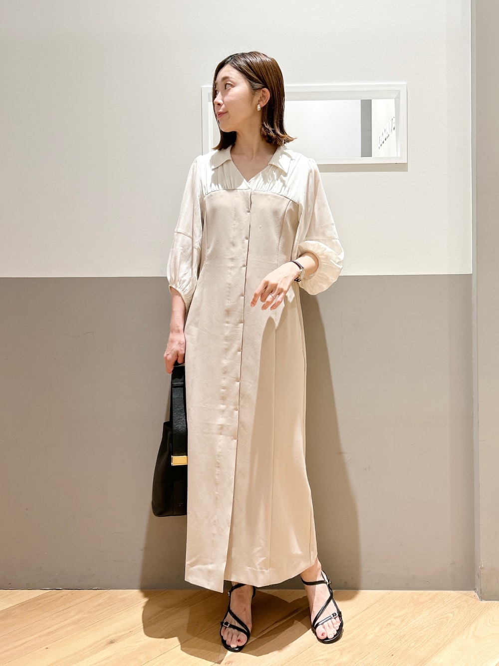 ベージュ系のワンピース、ブラック系のサンダル、ゴールド系のイヤリングを着用したレディースの春コーディネートの1枚目の写真