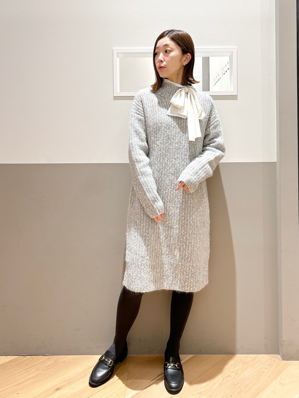 グレー系のワンピース、ホワイト系のシャツ/ブラウス、ブラック系のパンプスを着用したレディースの冬コーディネートの1枚目の写真