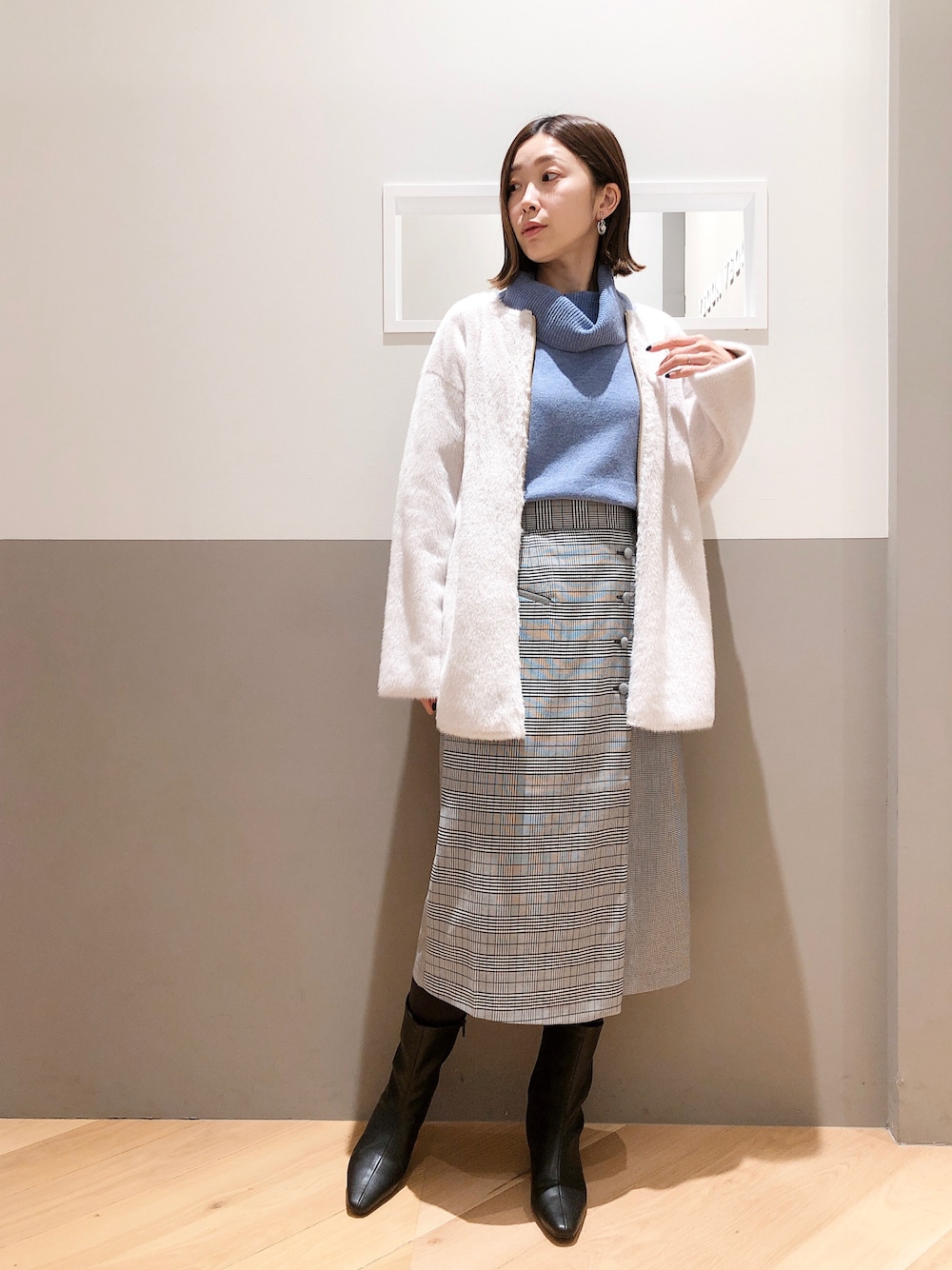 ベージュ系のノーカラーコート、ブルー系のニット/セーター、ブラック系のスカートを着用したレディースの冬コーディネートの1枚目の写真