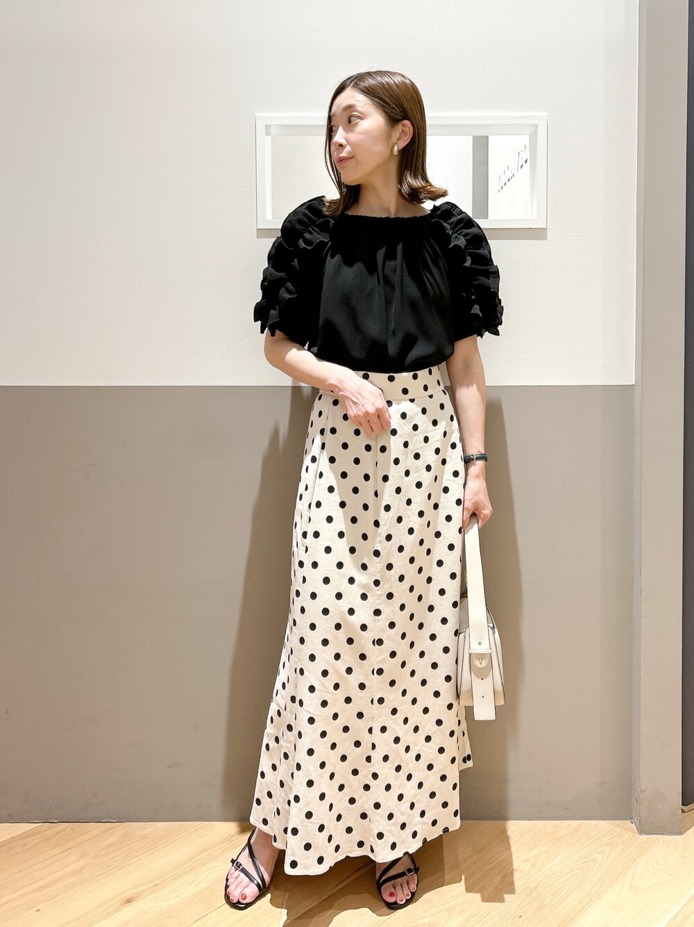 ブラック系のシャツ/ブラウス、ベージュ系のスカート、ブラック系のサンダルを着用したレディースの夏コーディネートの1枚目の写真