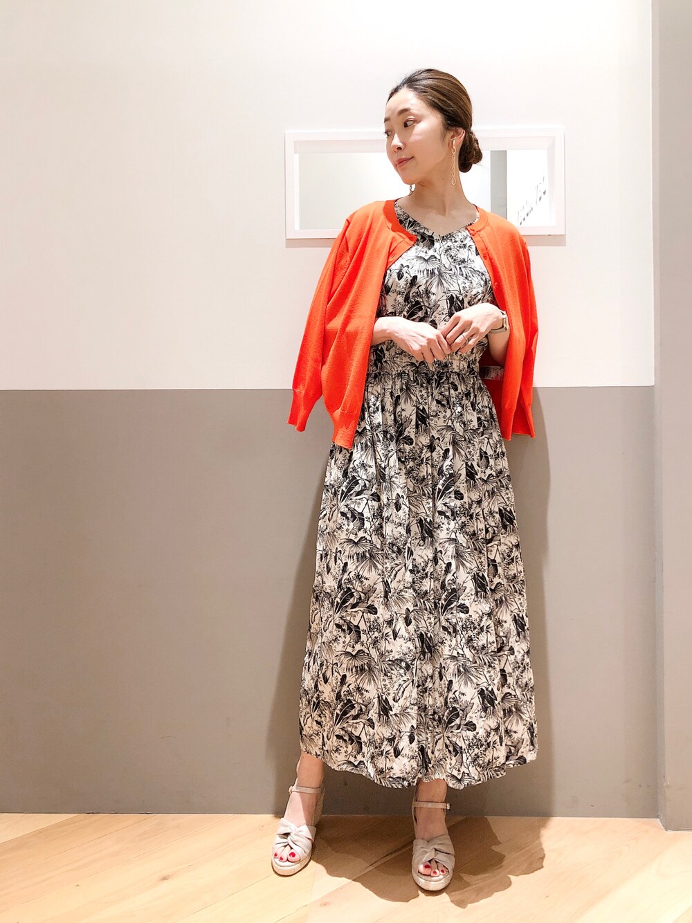 ブラック系のワンピース、オレンジ系のカーディガン/ボレロ、シルバー系のイヤリングを着用したレディースの夏コーディネートの1枚目の写真