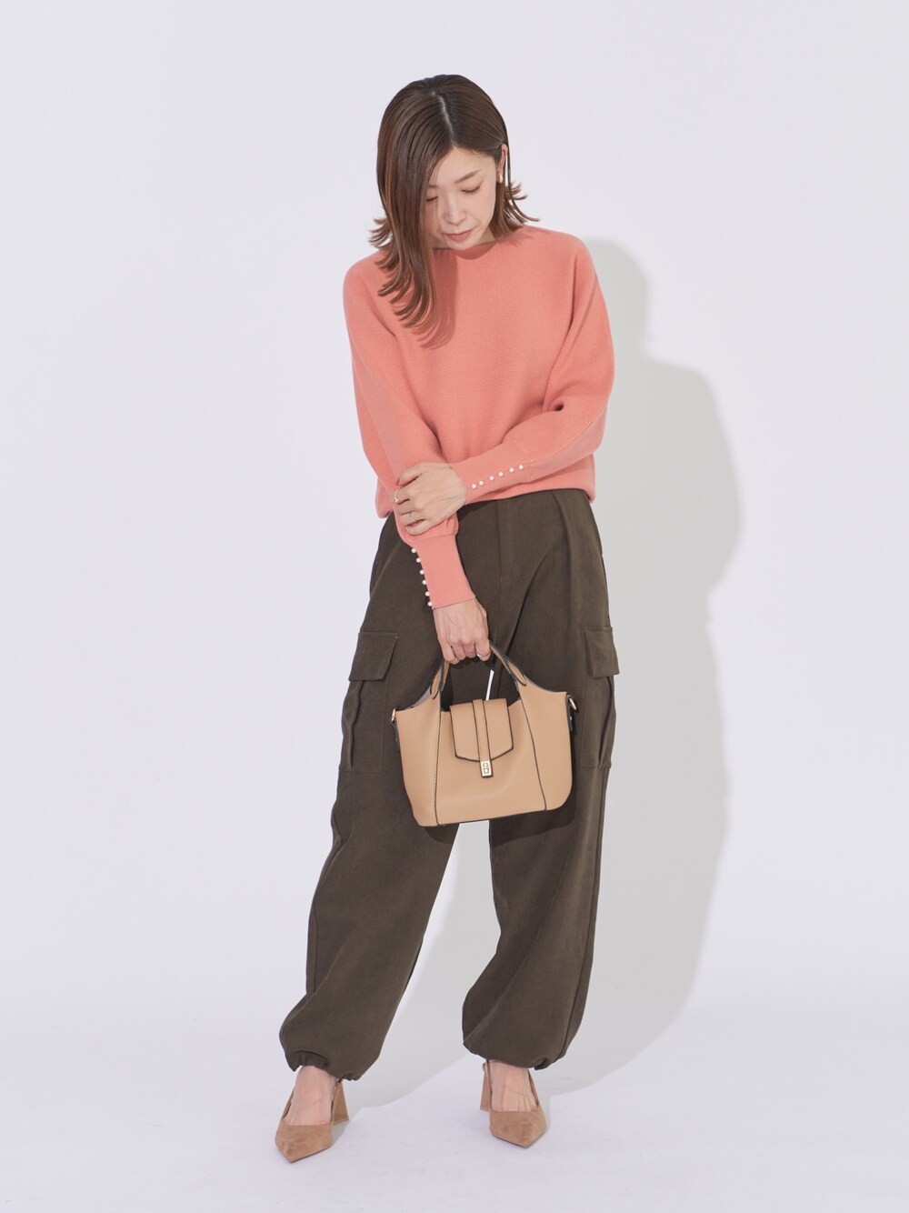 オレンジ系のニット/セーター、グリーン系のカーゴパンツ、ベージュ系のトートバッグを着用したレディースの冬コーディネートの1枚目の写真