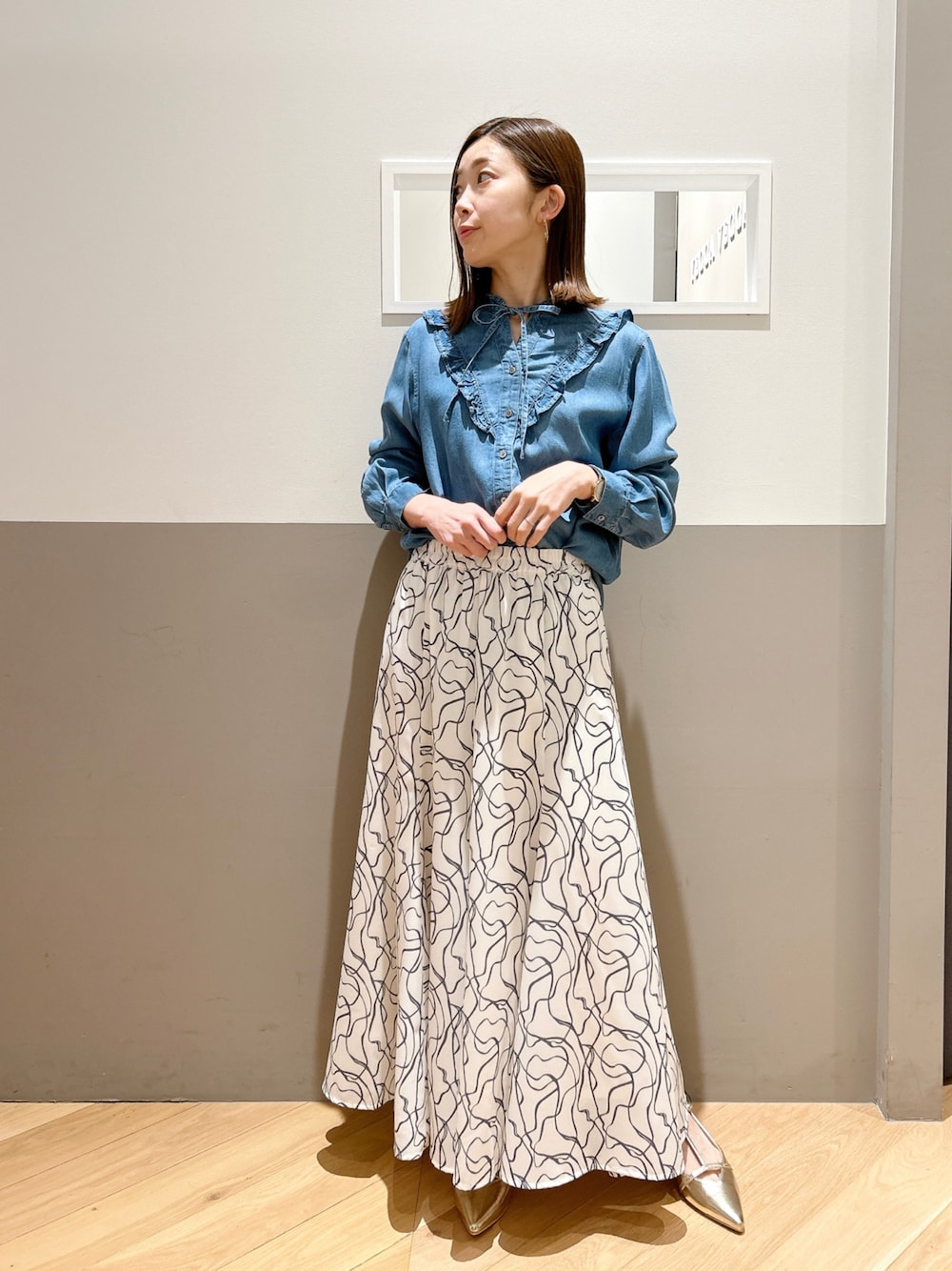 ブルー系のシャツ/ブラウス、ホワイト系のスカート、ゴールド系のパンプスを着用したレディースの冬コーディネートの1枚目の写真