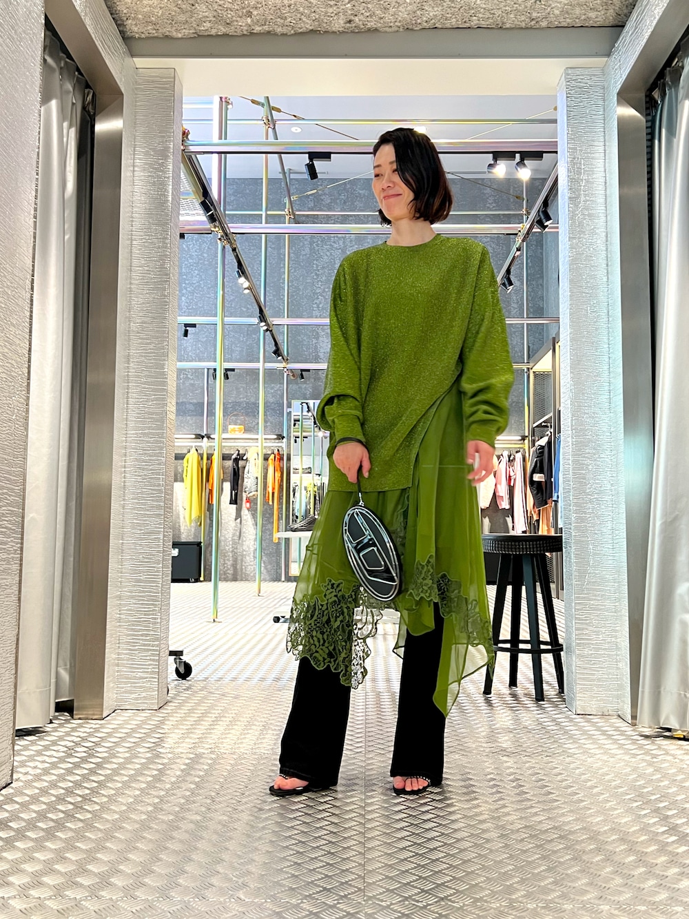 グリーン系のワンピース、ブラック系のショルダーバッグ、ブラック系のデニムパンツを着用したレディースの秋コーディネートの1枚目の写真