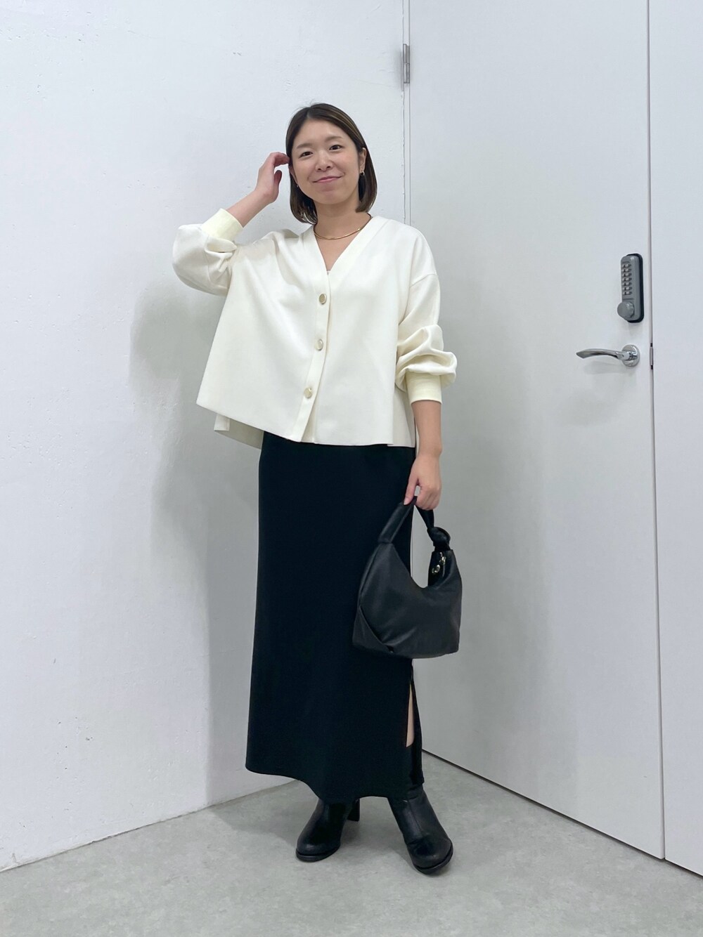 ホワイト系のカーディガン/ボレロ、ブラック系のスカート、ブラック系のショルダーバッグを着用したレディースの秋コーディネートの1枚目の写真