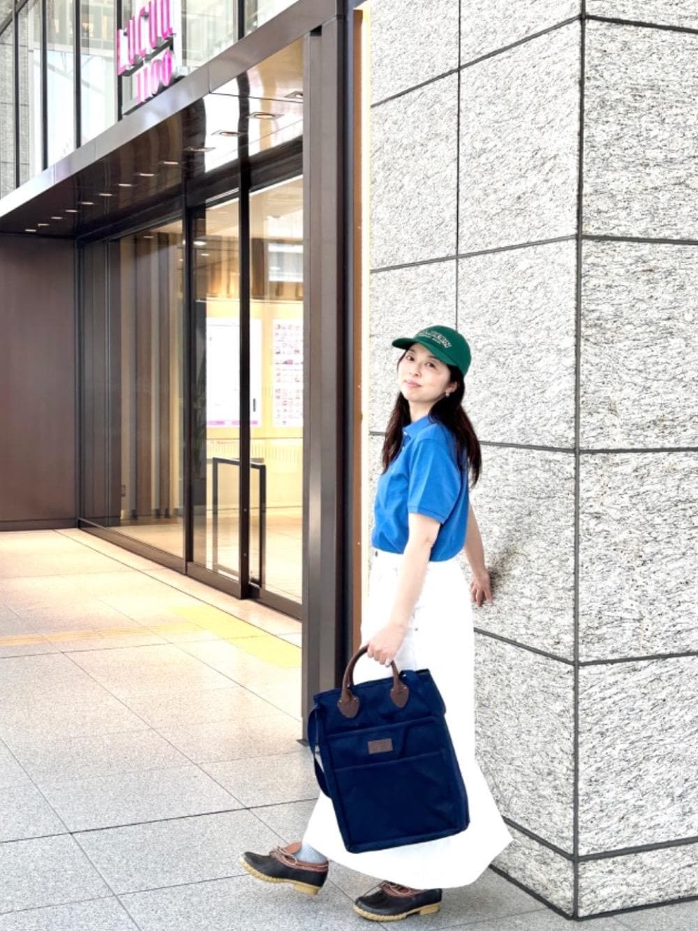 ブラウン系のモカシン/デッキシューズ、ブルー系のポロシャツ、ブルー系のトートバッグを着用したレディースの夏コーディネートの1枚目の写真