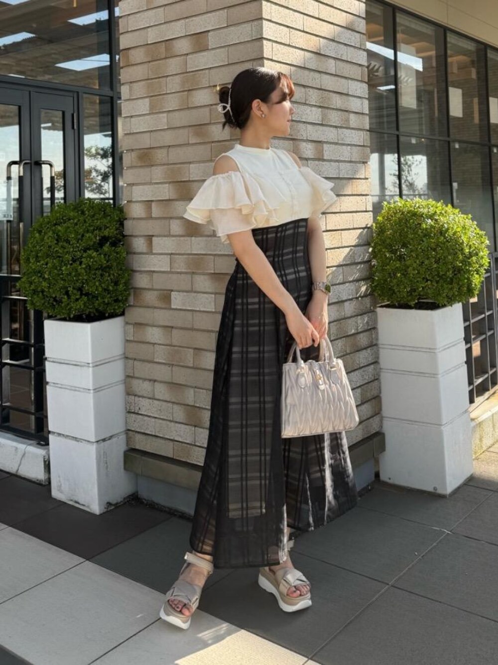 ベージュ系のサンダル、ベージュ系のハンドバッグ、ブラック系のワンピースを着用したレディースの夏コーディネートの1枚目の写真