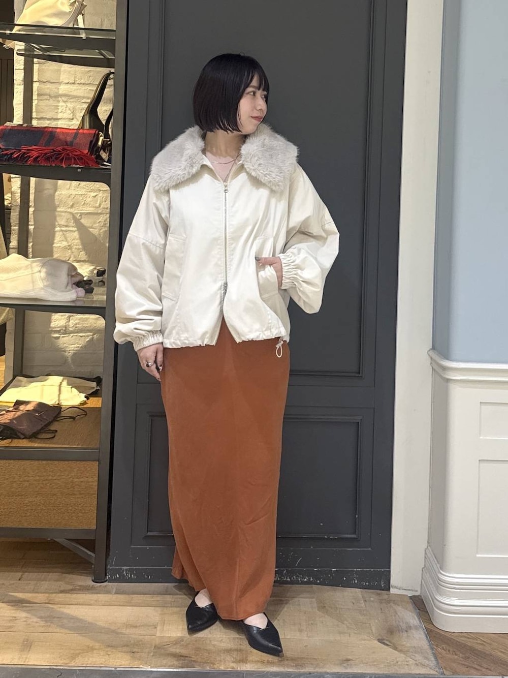 ブラック系のパンプス、ホワイト系のブルゾン、オレンジ系のスカートを着用したレディースの秋コーディネートの1枚目の写真