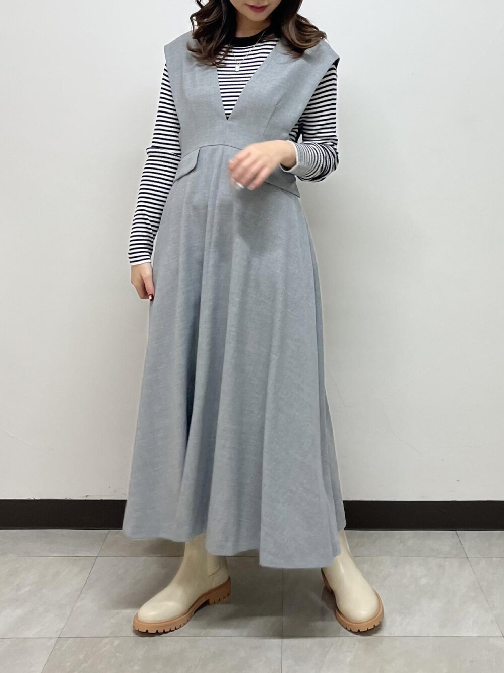 グレー系のジャンパースカート、ホワイト系のニット/セーター、ホワイト系のブーツを着用したレディースの冬コーディネートの1枚目の写真