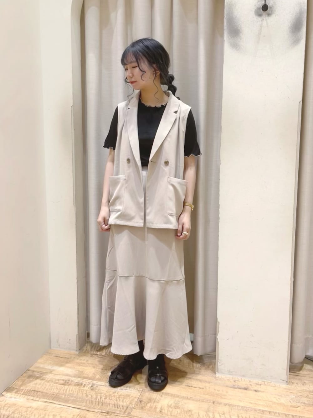 ベージュ系のベスト、ベージュ系のスカート、ブラック系のサンダルを着用したレディースの夏コーディネートの1枚目の写真